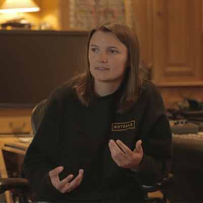 Person with long brown hair sitting in a darkened room in a dark hoodie