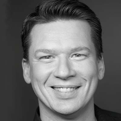 Professional headshot of person with short hair smiling in a dark t shirt