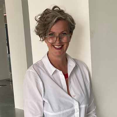 Person with short light hair and glasses smiling in white shirt