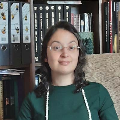 Person wearing glasses sitting in an armchair in front of a bookcase smiling