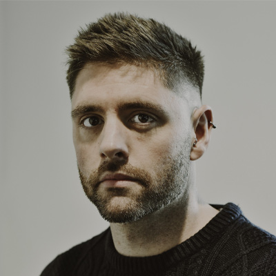 Headshot of person with beard, moustache and dark hair in black top