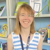 Person with bobbed light brown hair smiling at camera wearing blue and white striped top