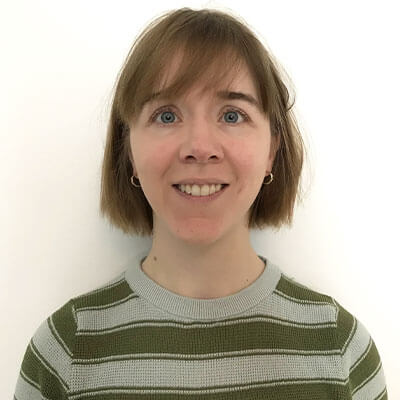 Person with bobbed light brown hair smiling at camera wearing grey and green striped jumper