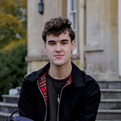 Young male student with curly brown hair sat on a bench.