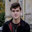 Young male student with curly brown hair sat on a bench.