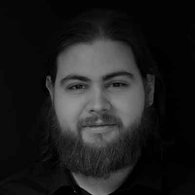 Headshot of person with beard, moustache and dark hair in black top