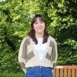A student stands in front of a green backdrop of trees and smiles at the camera
