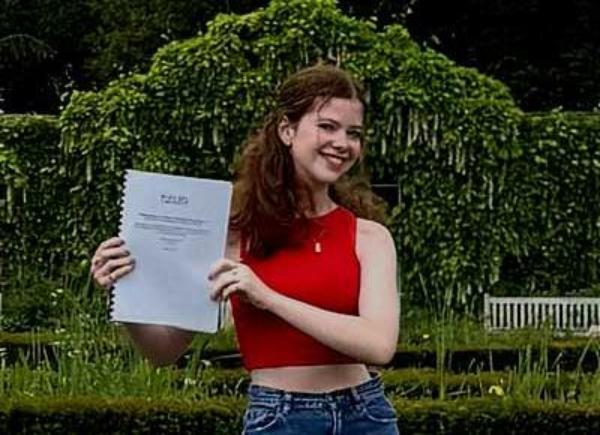 A person with long brown hair holds her dissertation up to the camera