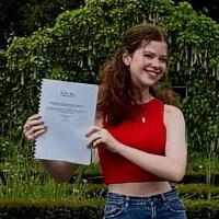 A person with long brown hair holds her dissertation up to the camera