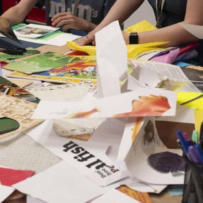 Table filled with art materials and hands playing with paper