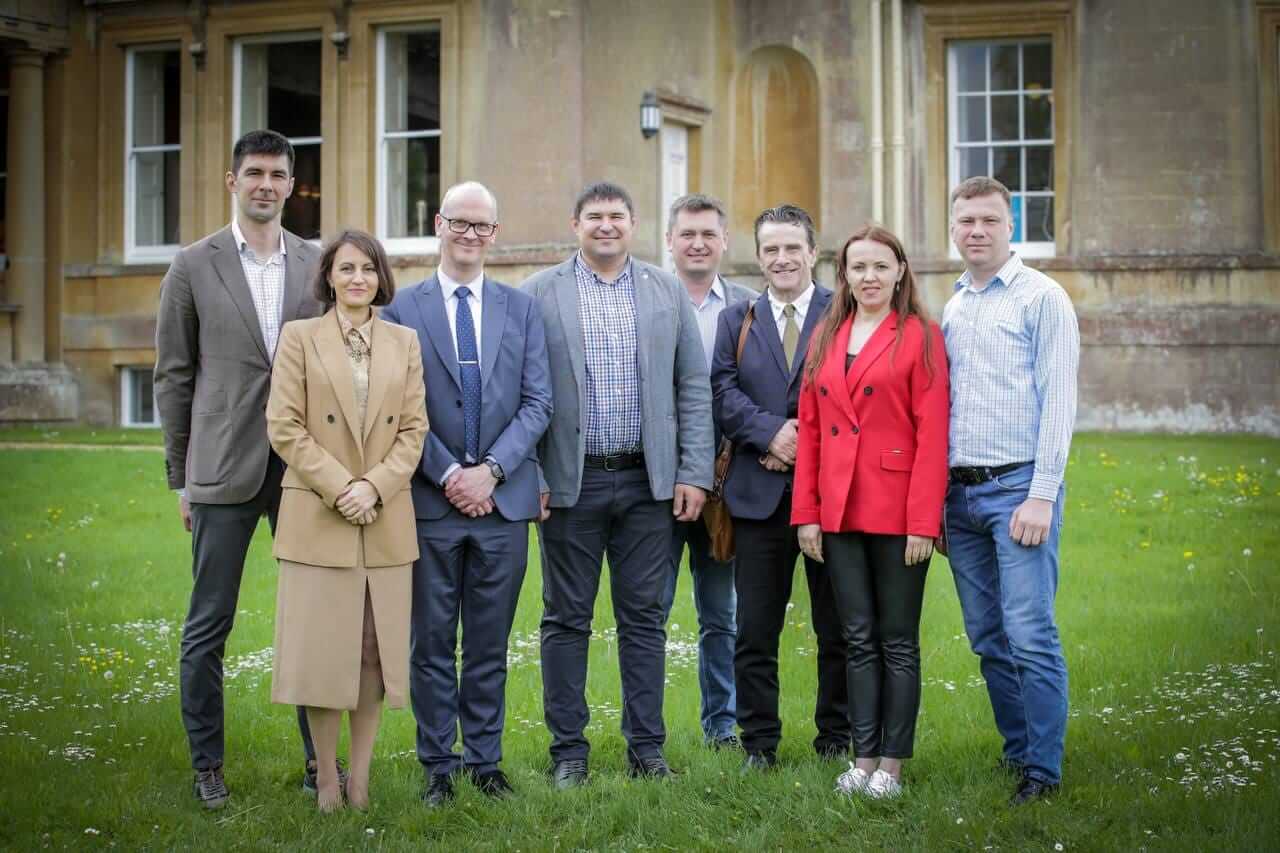 Eight people stand outside Main House and smile at the camera