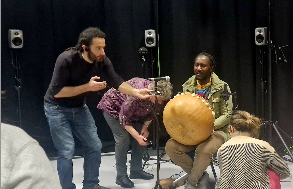 Three people stand around a binaural microphone to record sound