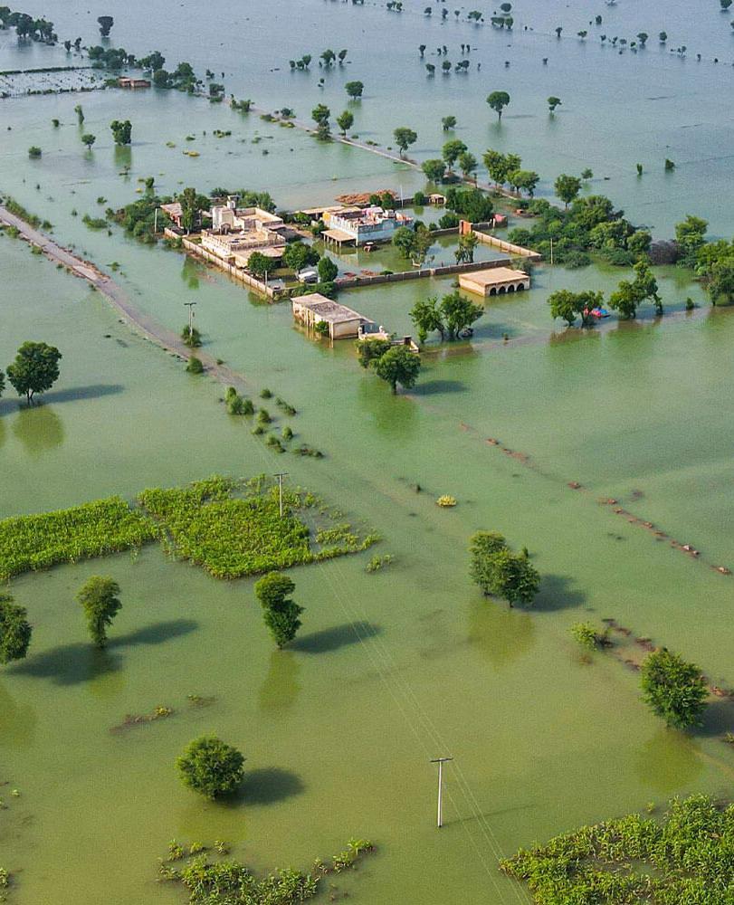 A vast flooded landscape of water over fields, with a few buildings and trees emerging from the still waters