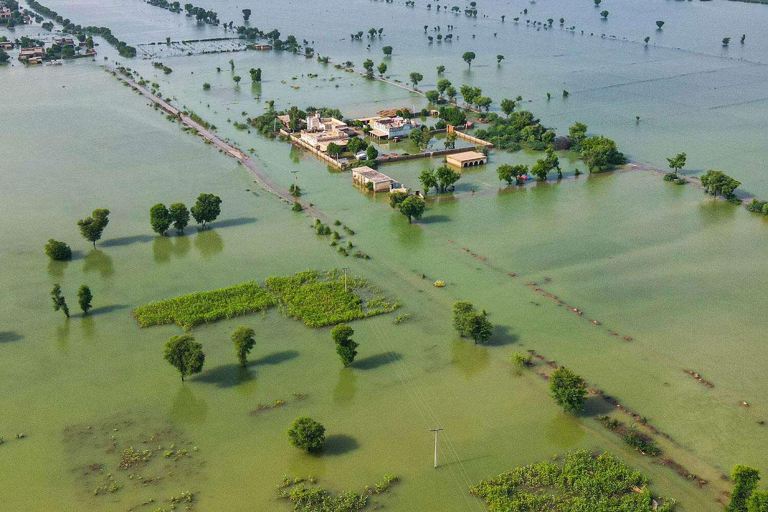 A vast flooded landscape of water over fields, with a few buildings and trees emerging from the still waters