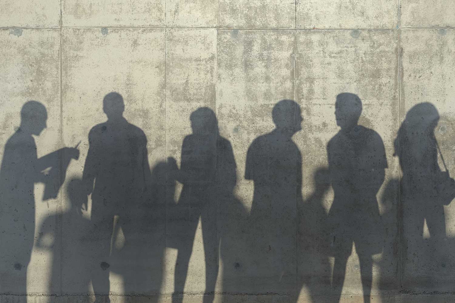 A group of people stand in front of a concrete wall, casting shadows