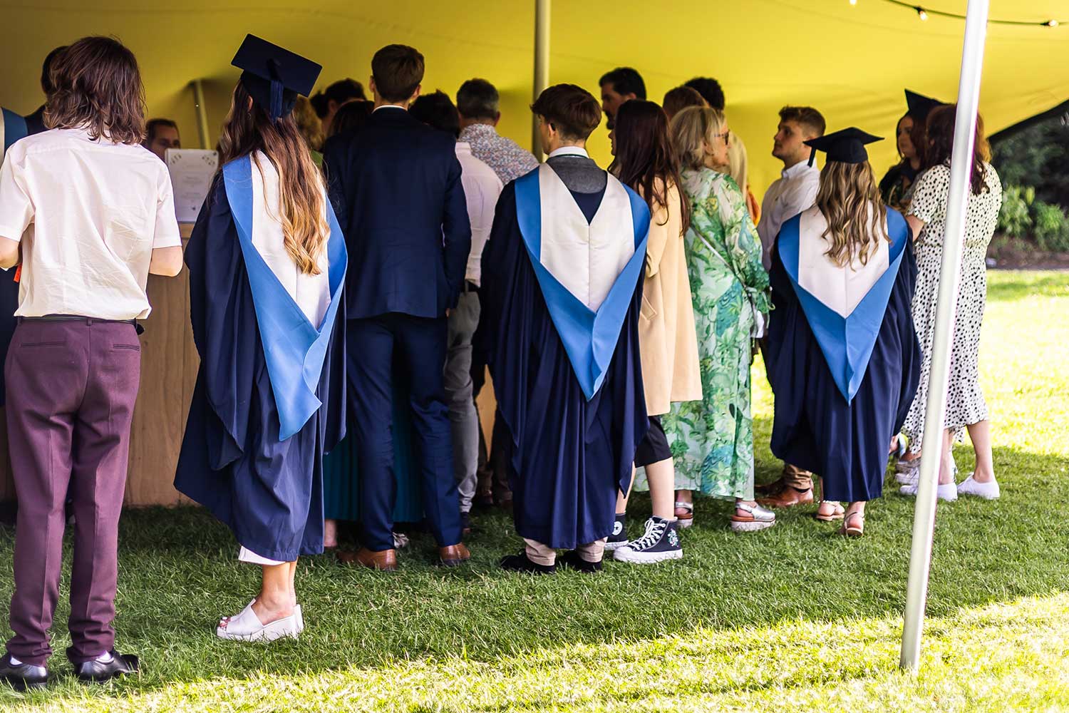 Graduates and their guests line up at a bar inside a marquee