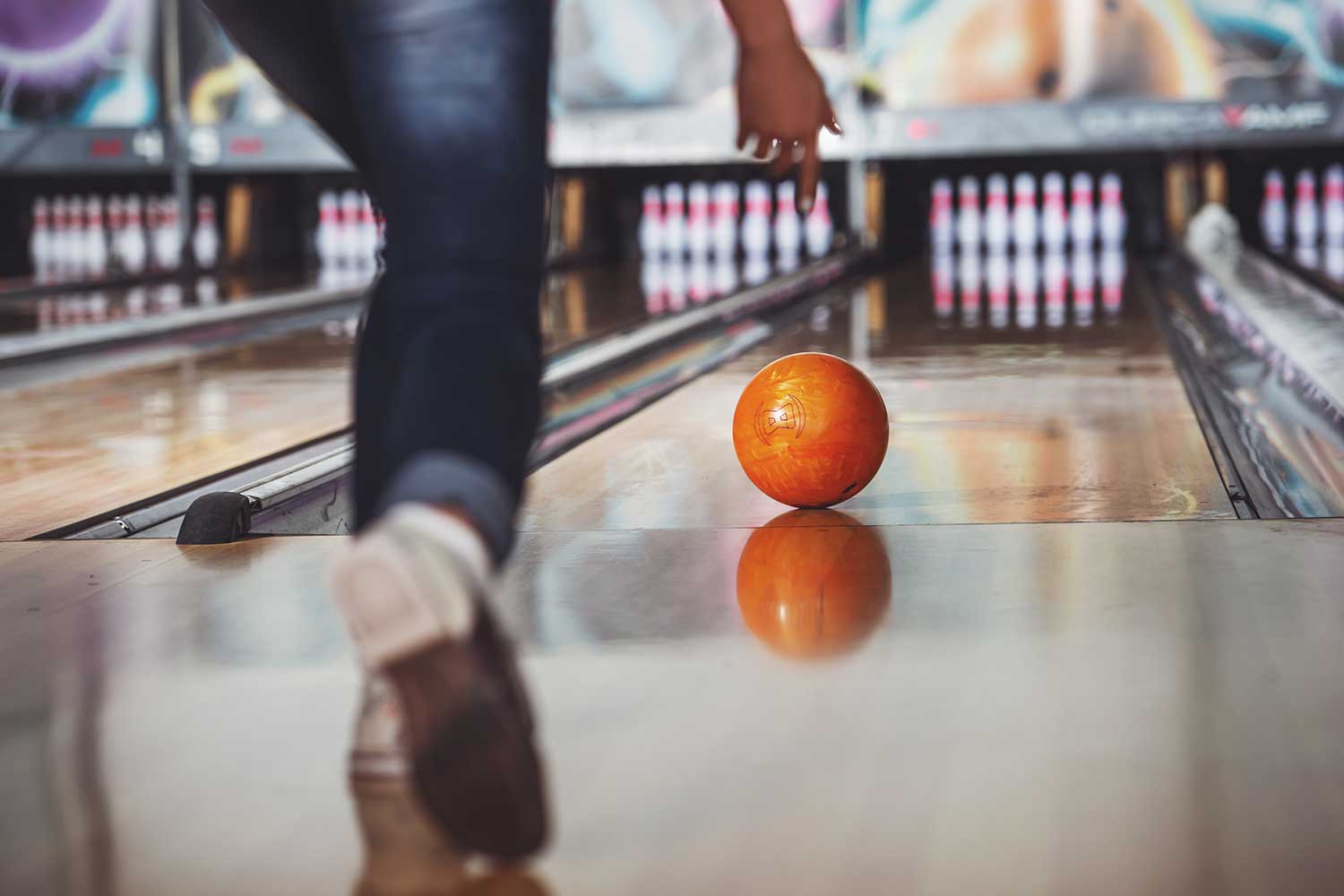 A person rolls a bowling ball down an alley