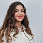 Woman with wavy brown hair and wearing a cream suit jacket smiles at the camera