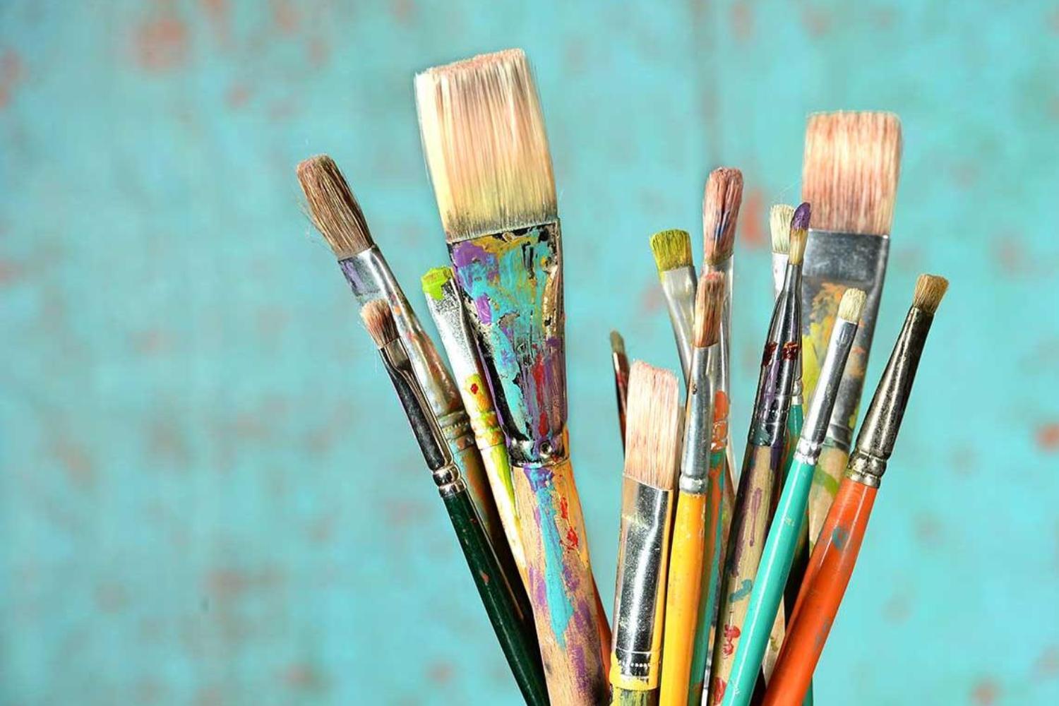 A jar or paintbrushes sits in front of a teal backdrop